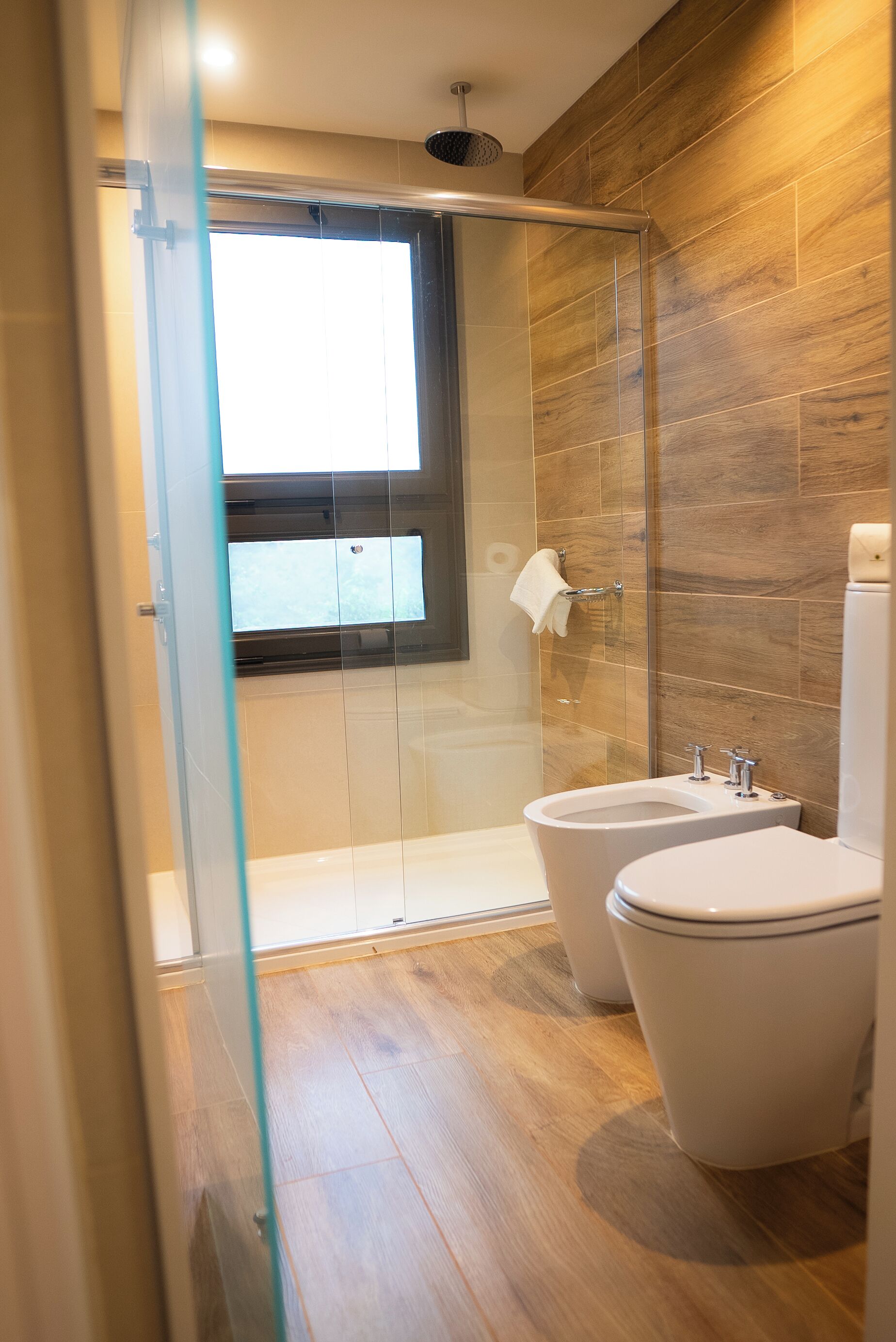 A modern bathroom with a glass shower enclosure, a toilet, and a bidet.