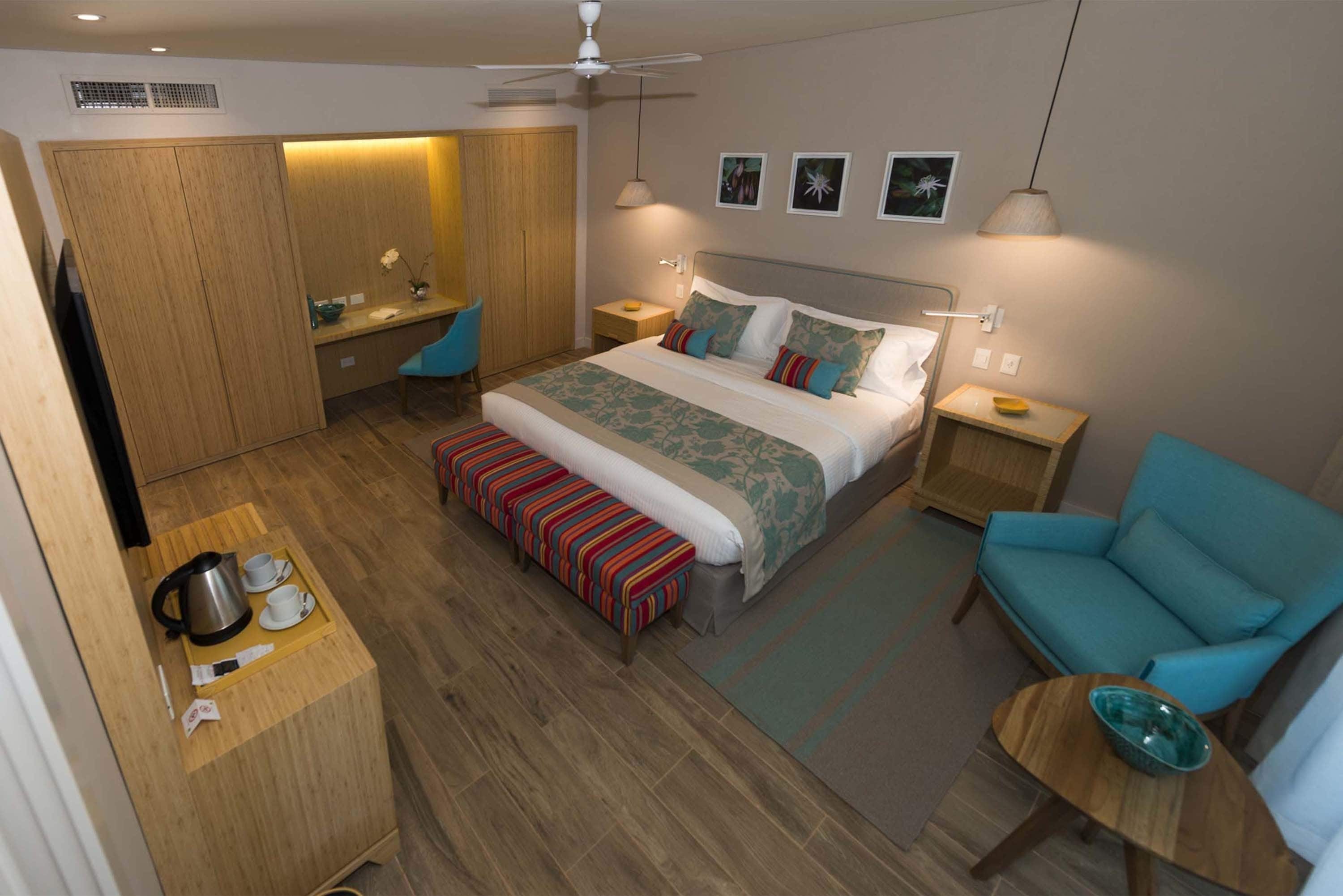 A modern hotel room with a bed, a desk, a chair, a sofa, and a small table.