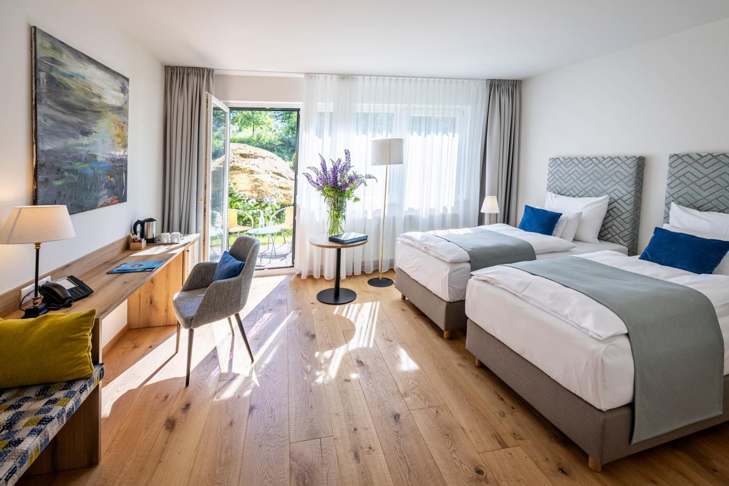 Habitación de hotel con dos camas, un escritorio, una silla y vistas al exterior.