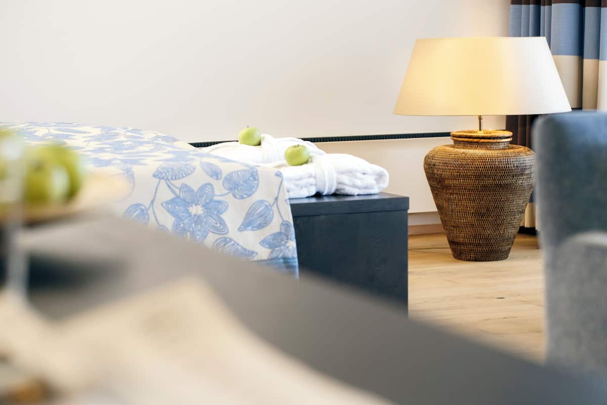 A hotel room with a bed, a lamp, a chair, and a small table with apples.