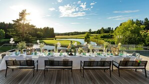 Une terrasse avec une table dressée pour un repas, offrant une vue sur un lac et un terrain de golf.