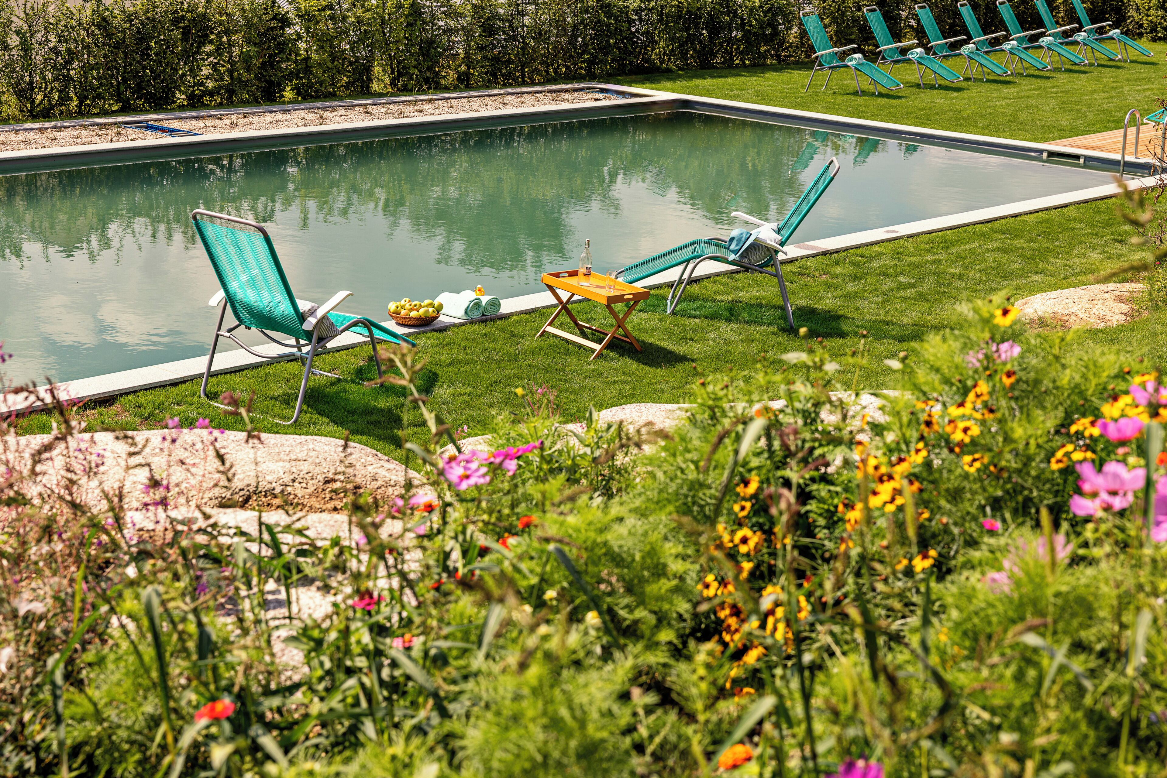 A swimming pool with lounge chairs, a table, and a grassy area with flowers.