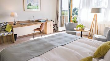 A hotel room with a bed, a desk with a chair, a small table with a lamp, and a view of the outdoors.