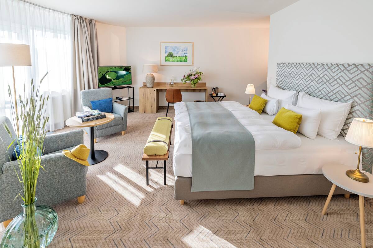 A hotel room with a bed, a desk, a chair, a TV, and a window with curtains.