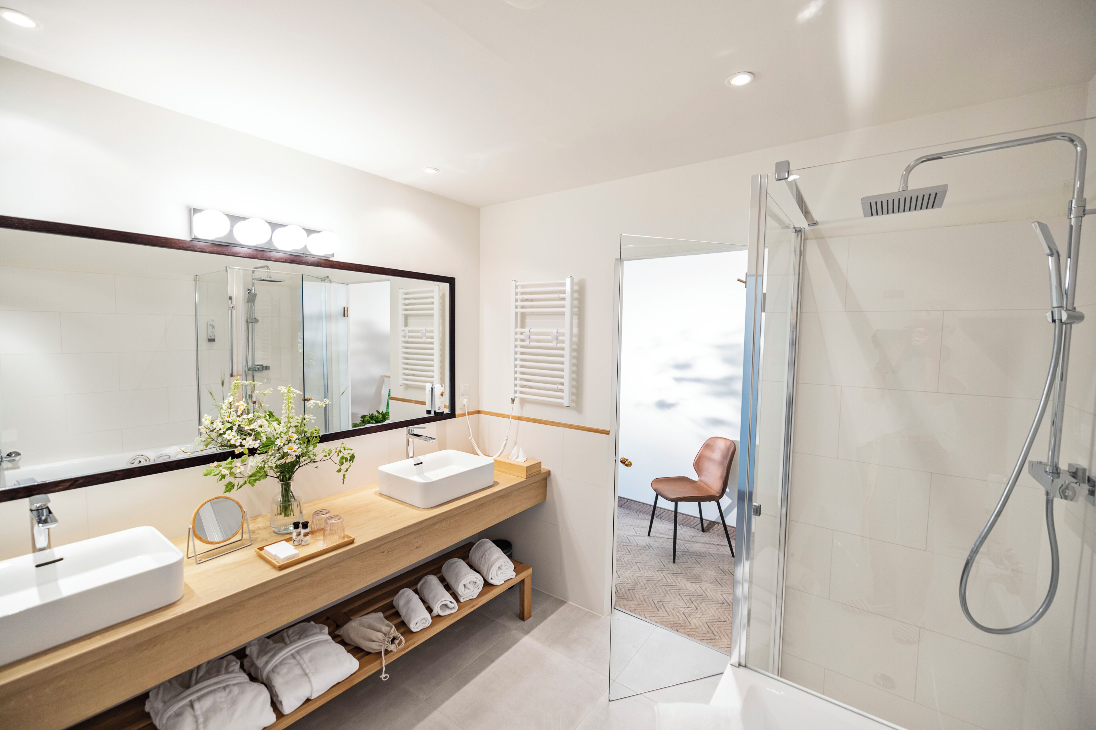 Un baño moderno con un espejo grande, dos lavamanos, una ducha y un mueble de tocador de madera.