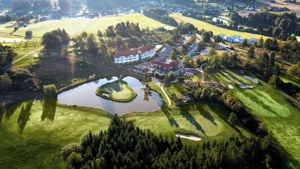 Un parcours de golf doté de bunkers, d’un étang et d’un club-house.