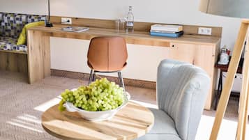 A modern living room with a round wooden table, a grey armchair, and a sofa. There is a bowl of green grapes on the table.