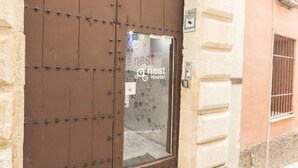 A brown metal door with a glass panel, a small sign, and a manhole cover on the ground. - White Nest (Granada)