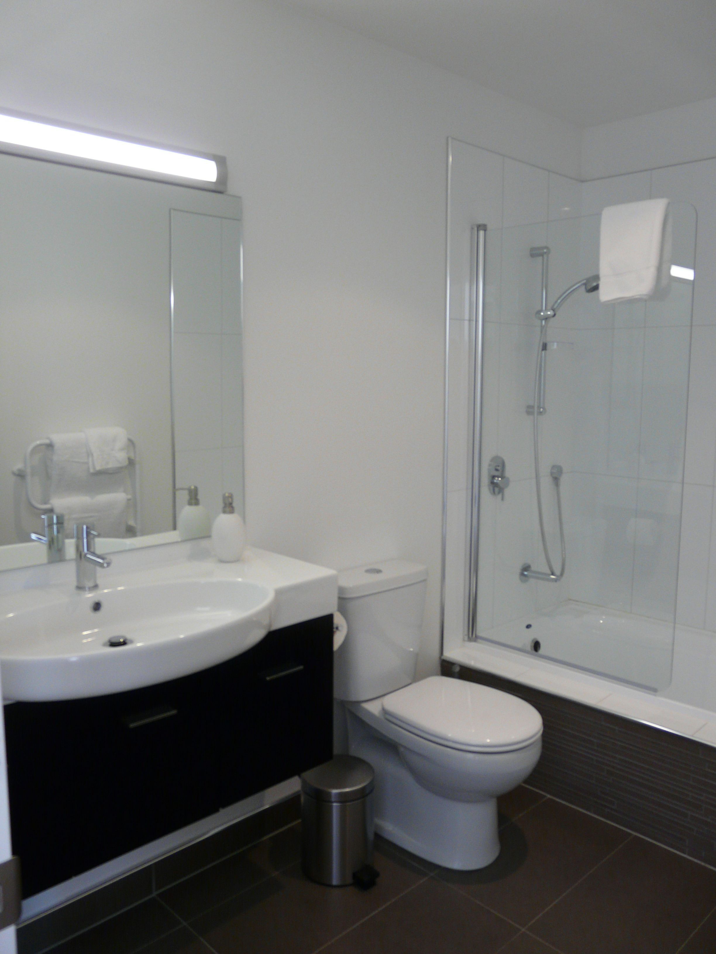 Un baño moderno con lavamanos, inodoro y ducha con mampara de vidrio.