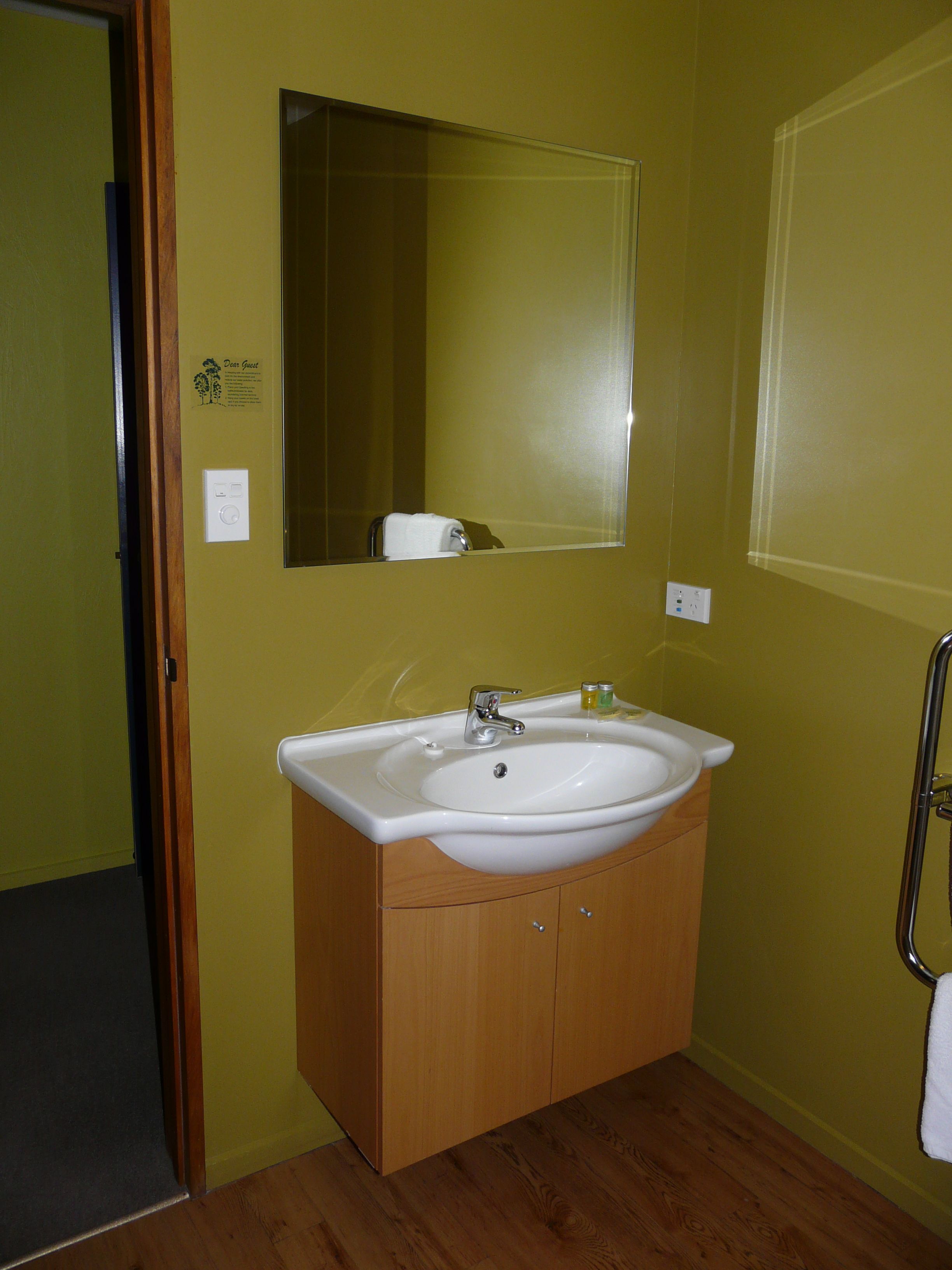 Un baño con lavamanos blanco, mueble de madera y un espejo grande.