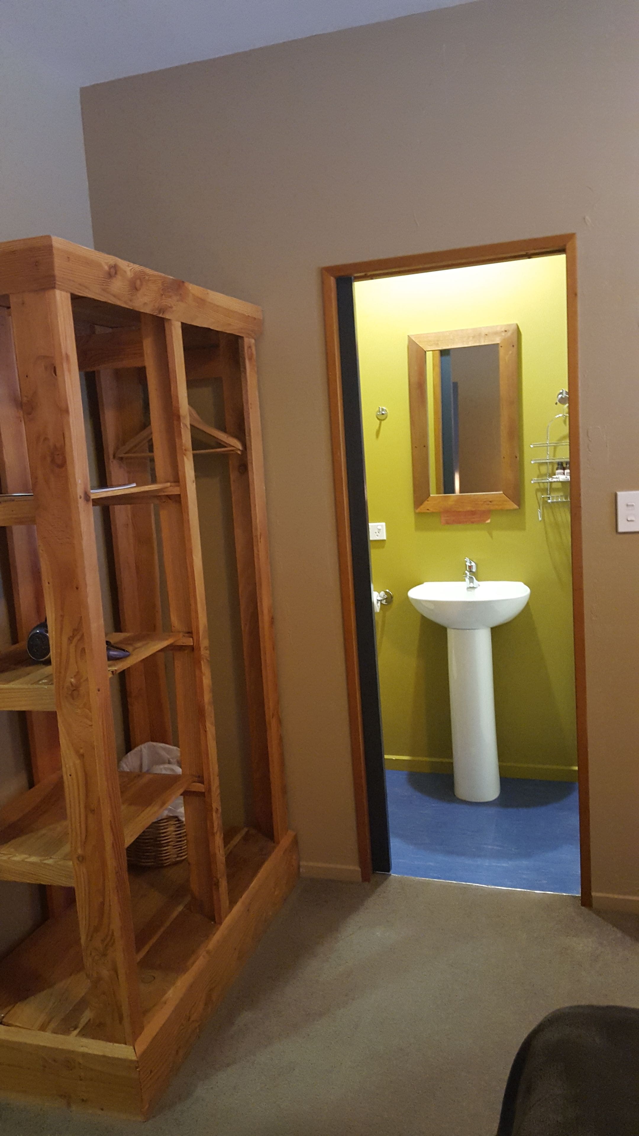 A room with a wooden shelving unit and a bathroom with a sink and mirror.