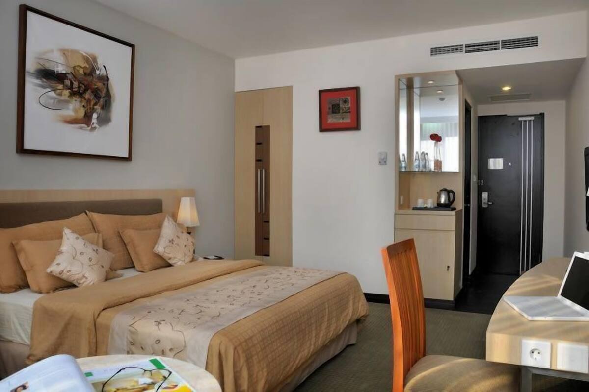 Hotellihuone, jossa on sänky, työpöytä, tuoli, peili ja taulu seinällä.