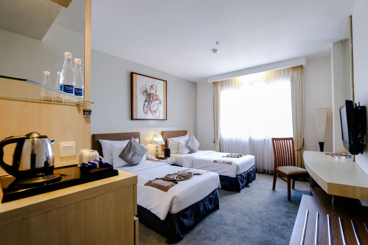 Hotellihuone, jossa on kaksi sänkyä, työpöytä, tuoli, televisio ja kahvinkeitin.
