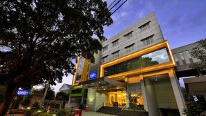 Un hotel moderno con fachada de vidrio, zona de estar al aire libre y una escalera que conduce a la entrada.