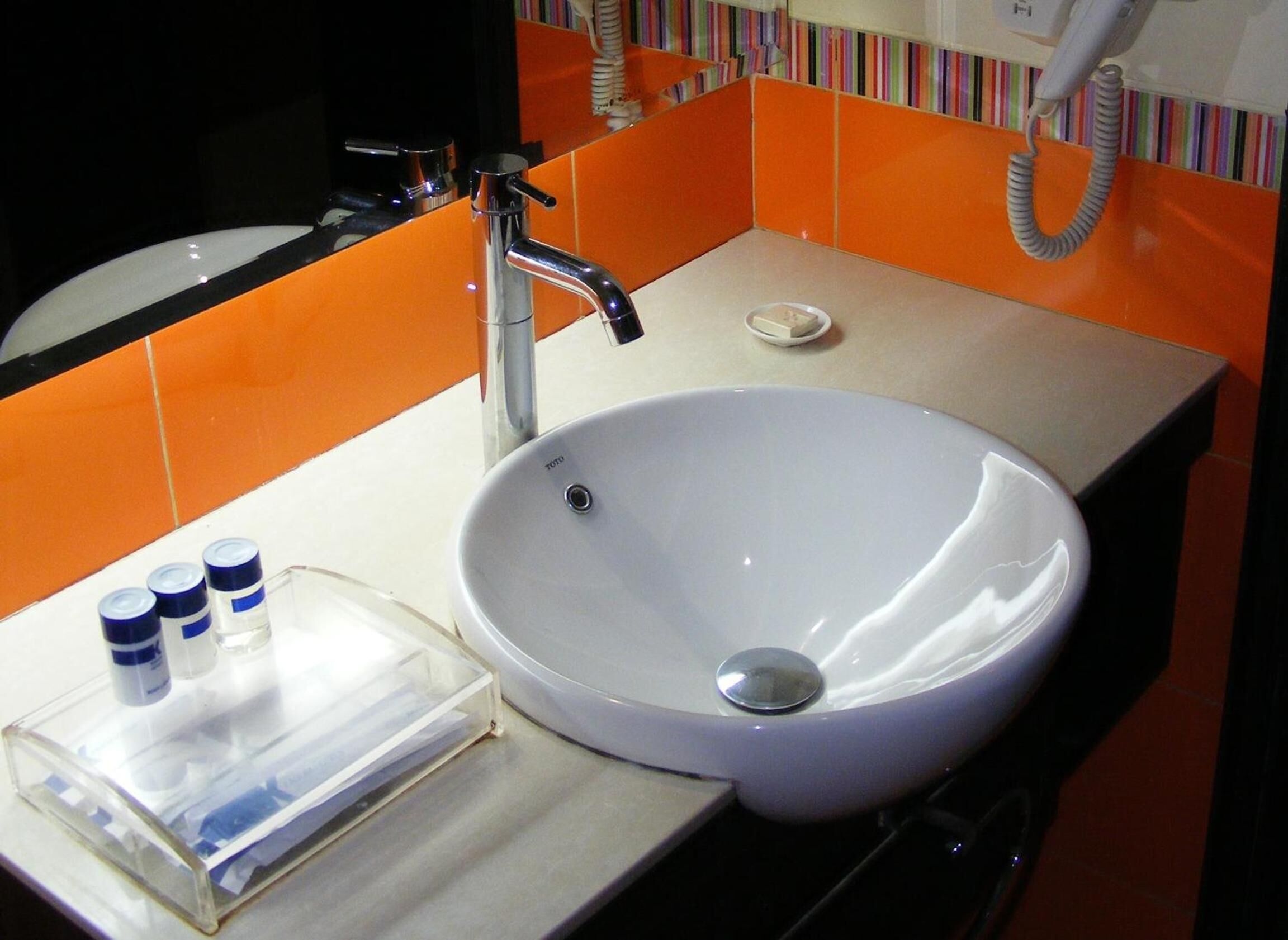 A bathroom with a white sink, a mirror, and orange tiled walls.