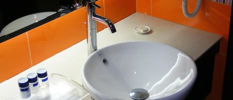 Un baño con un lavamanos blanco, un espejo y paredes con azulejos naranjas.