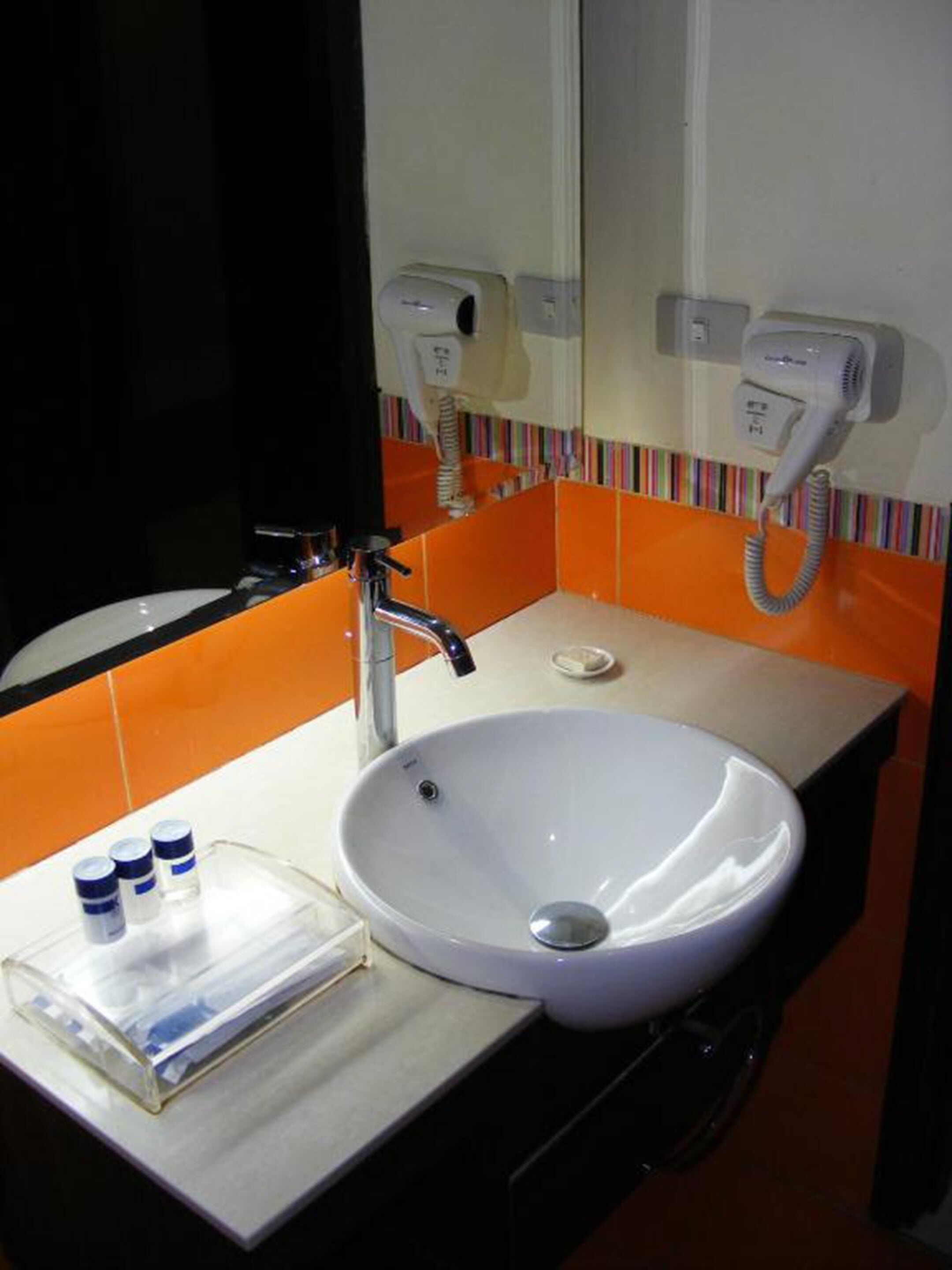 Un baño con un lavabo blanco, un espejo y una pared de azulejos naranjas.