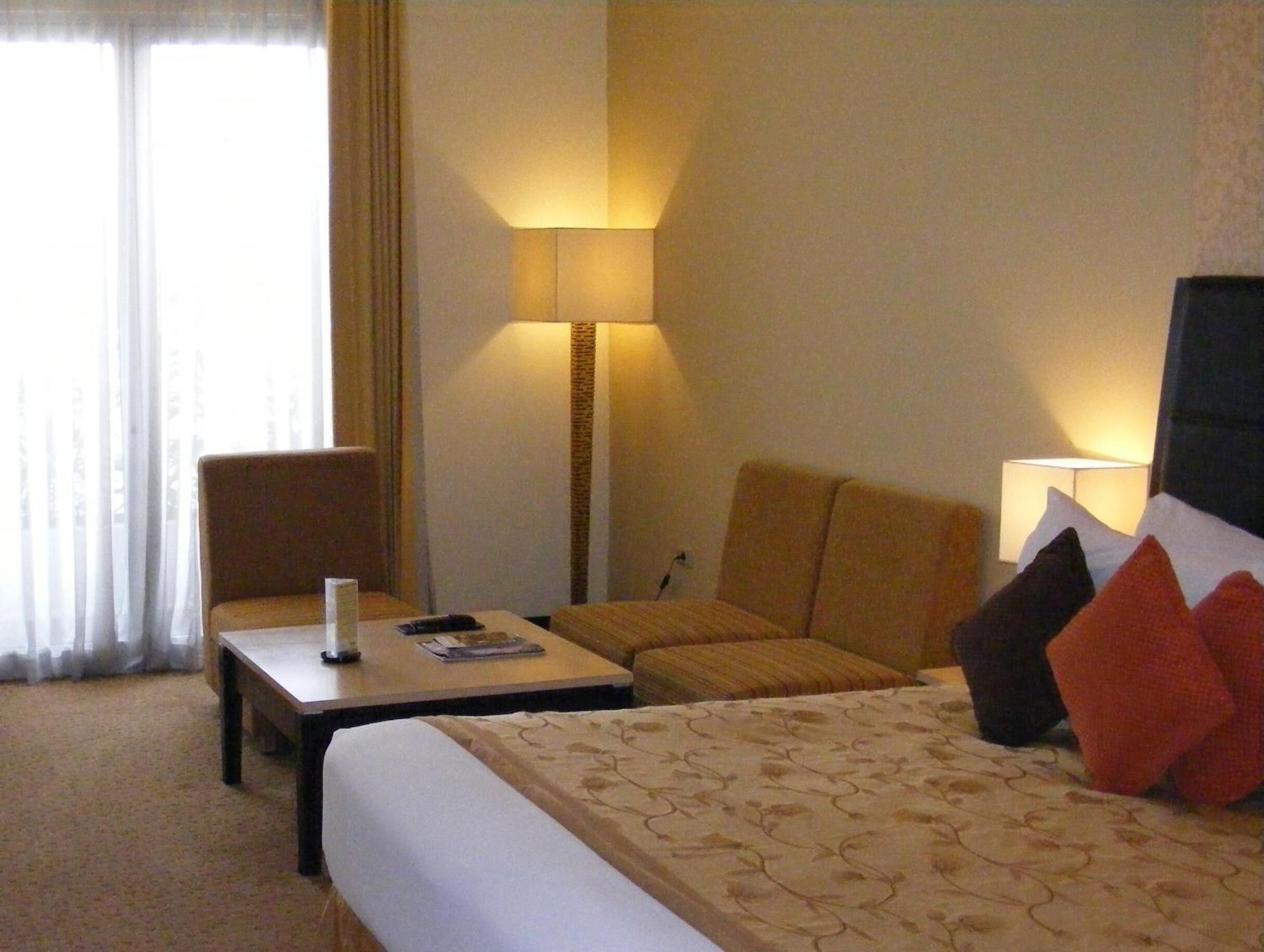 A hotel room with a bed, a desk, a chair, a lamp, and a window with curtains.