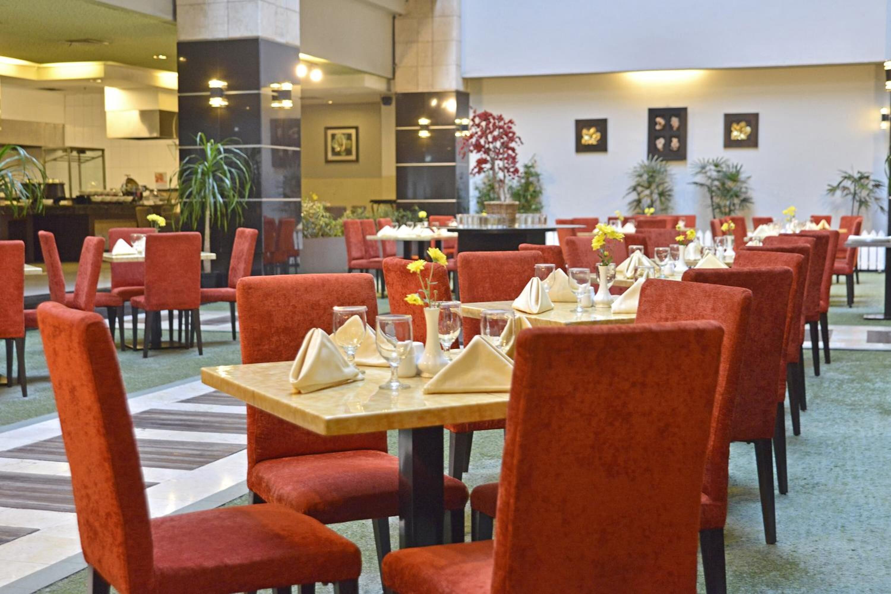 A hotel dining area with red upholstered chairs and tables set with white napkins and glassware.
