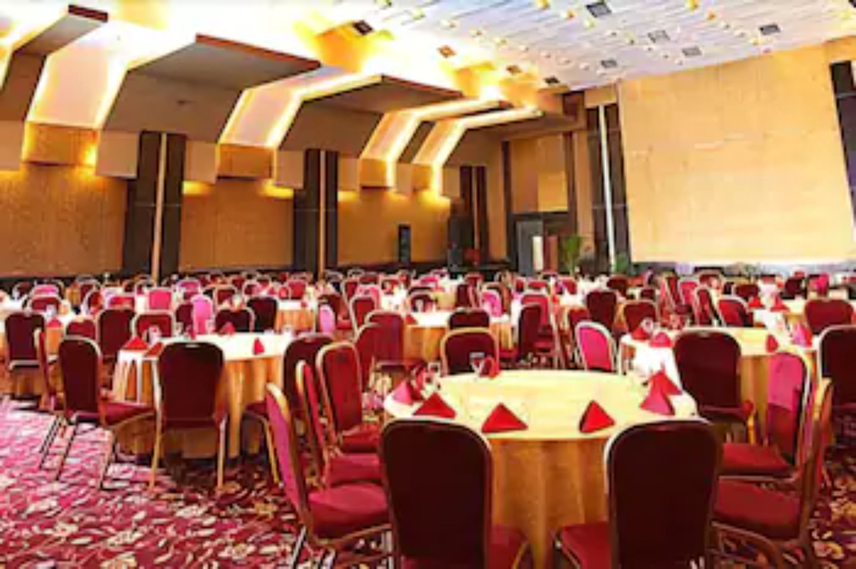 A large banquet hall with round tables and red chairs, arranged in rows.