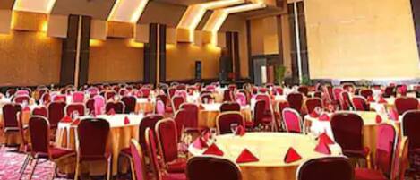 A large banquet hall with round tables and red chairs, arranged in rows.
