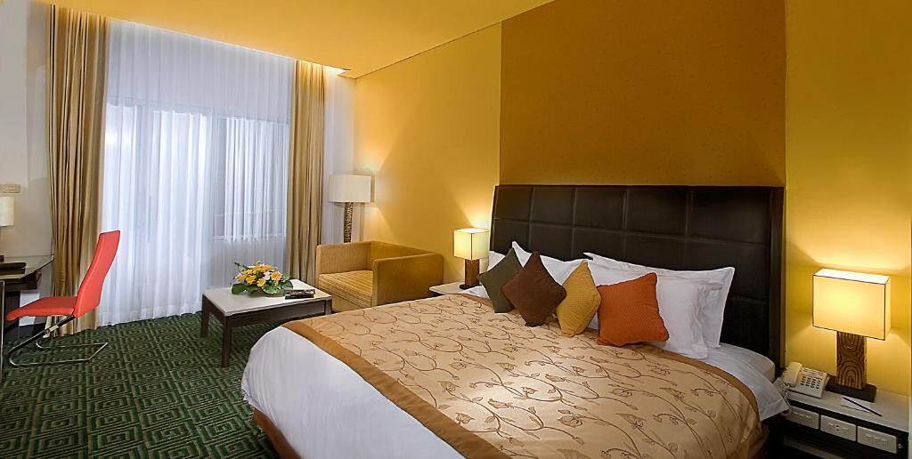 A hotel room with a large bed, a desk, a chair, and a window with curtains.