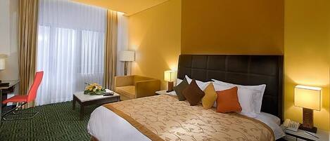 A hotel room with a large bed, a desk, a chair, and a window with curtains.
