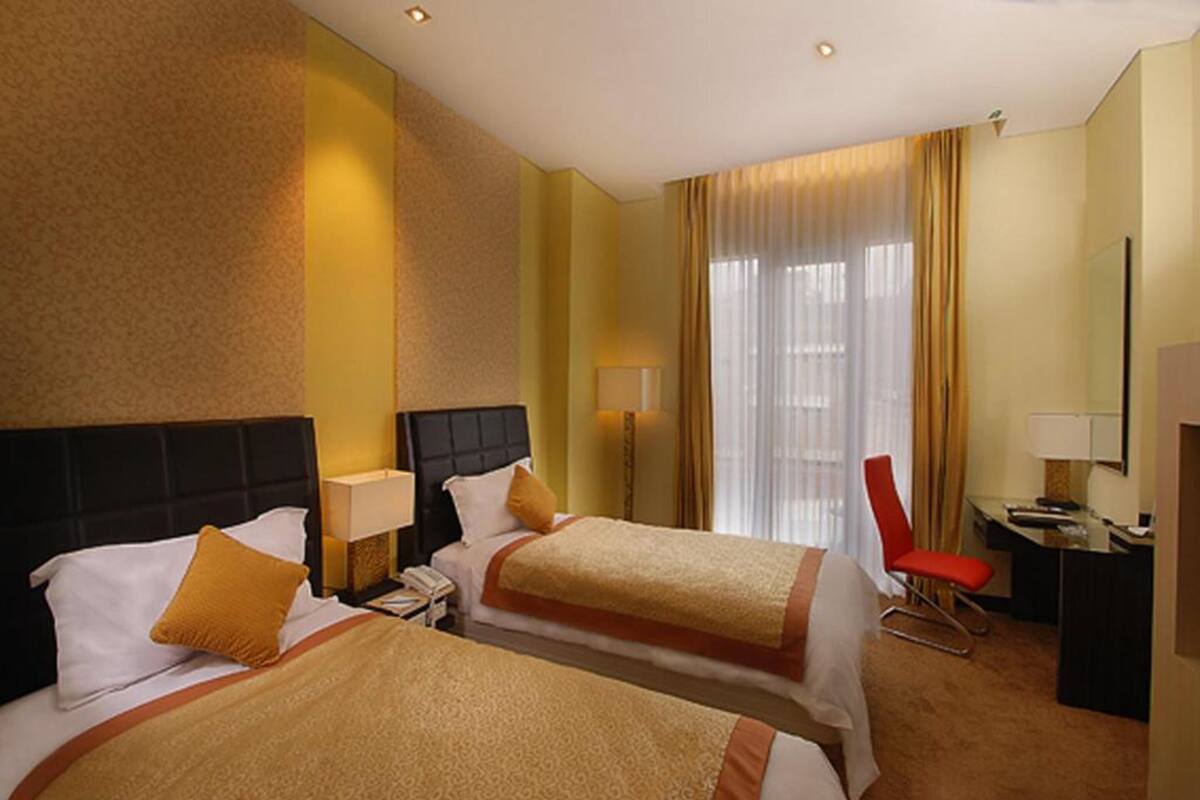 Een hotelkamer met twee bedden, een bureau, een stoel en een groot raam met gordijnen.
