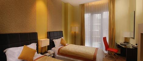 A hotel room with two beds, a desk, a chair, and a large window with curtains.
