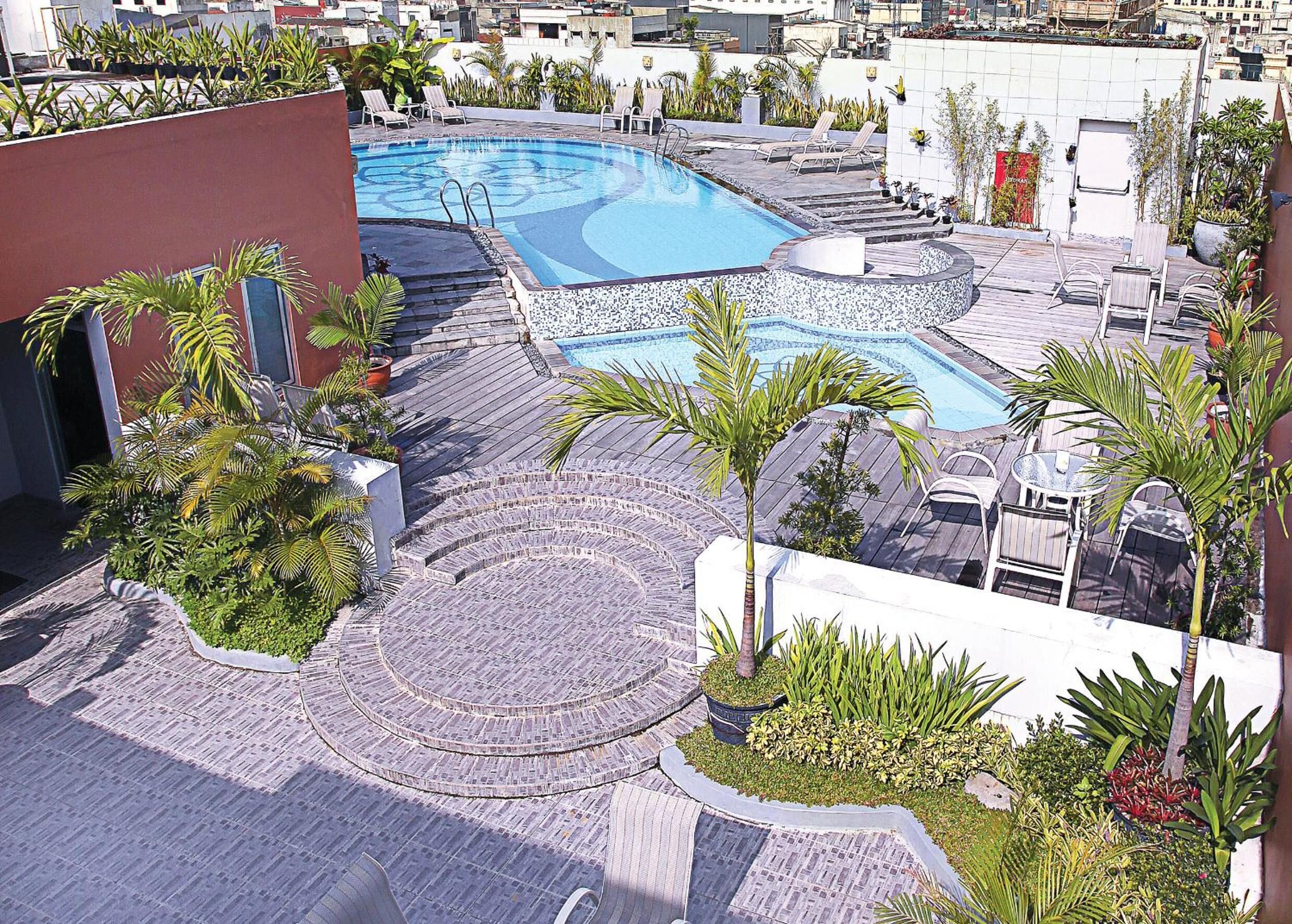 A rooftop pool area with multiple pools, surrounded by palm trees and lounge chairs.