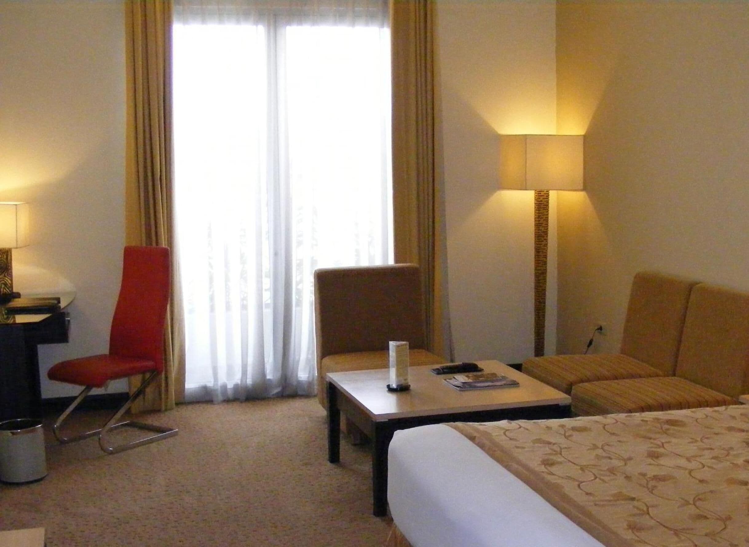 A hotel room with a bed, two armchairs, a small table, a lamp, and a window with curtains.