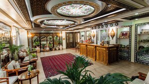 Um hall espaçoso com designs ornamentais no teto, uma receção em madeira central e diversas áreas de estar.