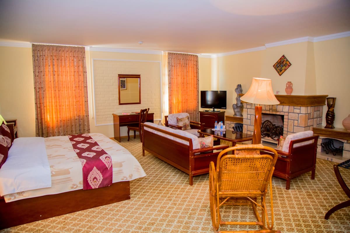 A hotel room with a bed, sofa, chairs, a television, and a fireplace.