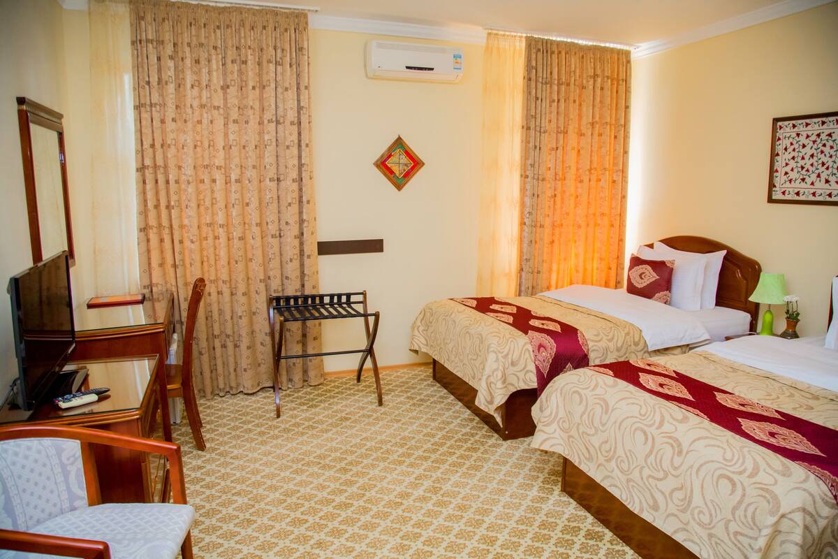 A hotel room with two beds, a desk with a chair, a television, and an air conditioning unit.