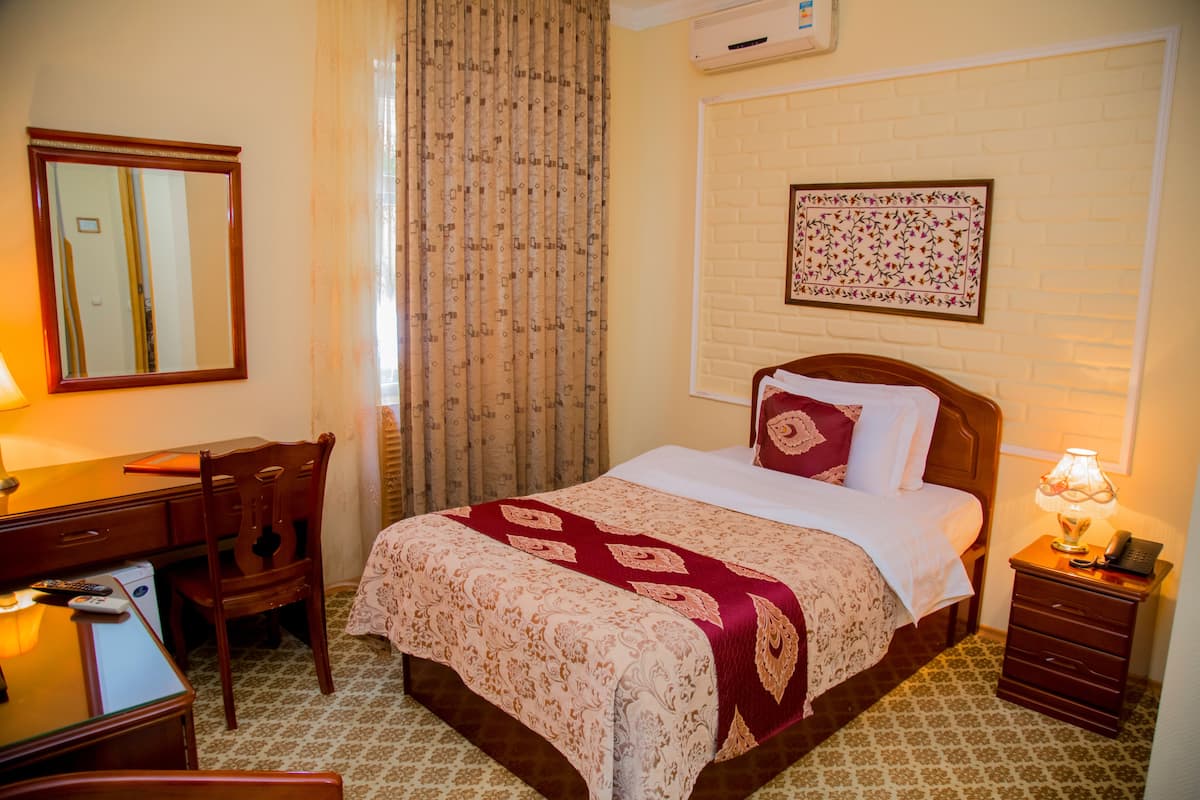 A hotel room with a bed, a desk, a chair, a nightstand, and a wall-mounted air conditioner.