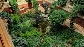 Pátio com edifício de tijolos, plantas verdes e um pequeno espelho d'água.