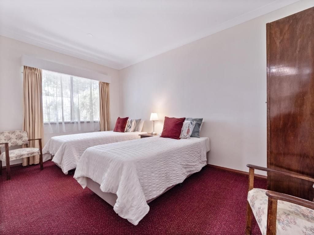 Una habitación de hotel con dos camas, un armario de madera, una silla y un ventanal con cortinas.