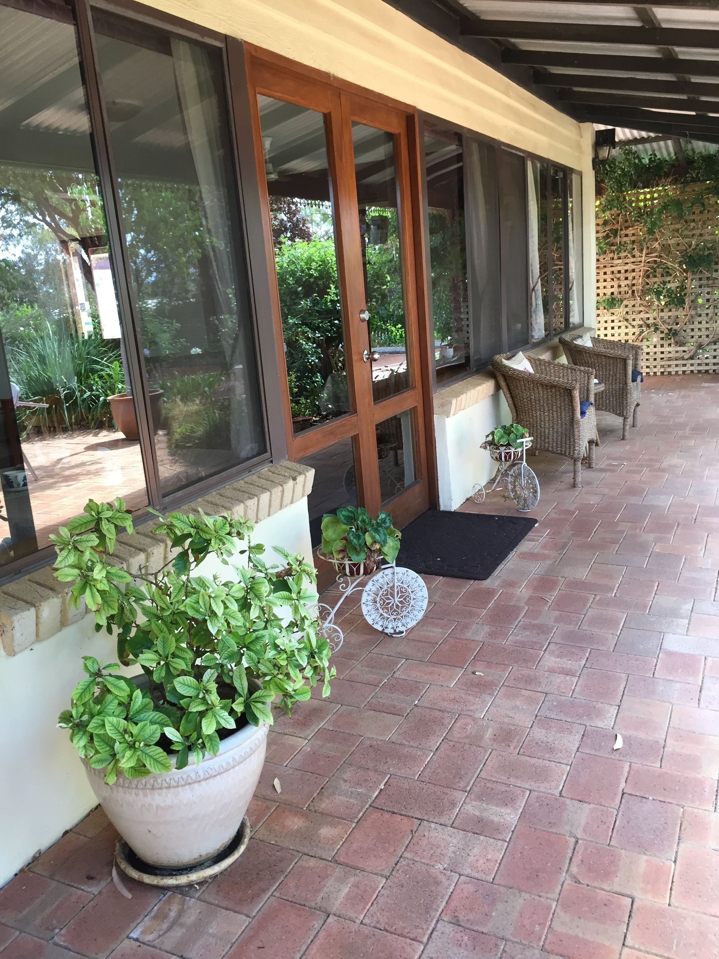 A covered patio area with potted plants, wicker furniture, and a view of the surrounding greenery.