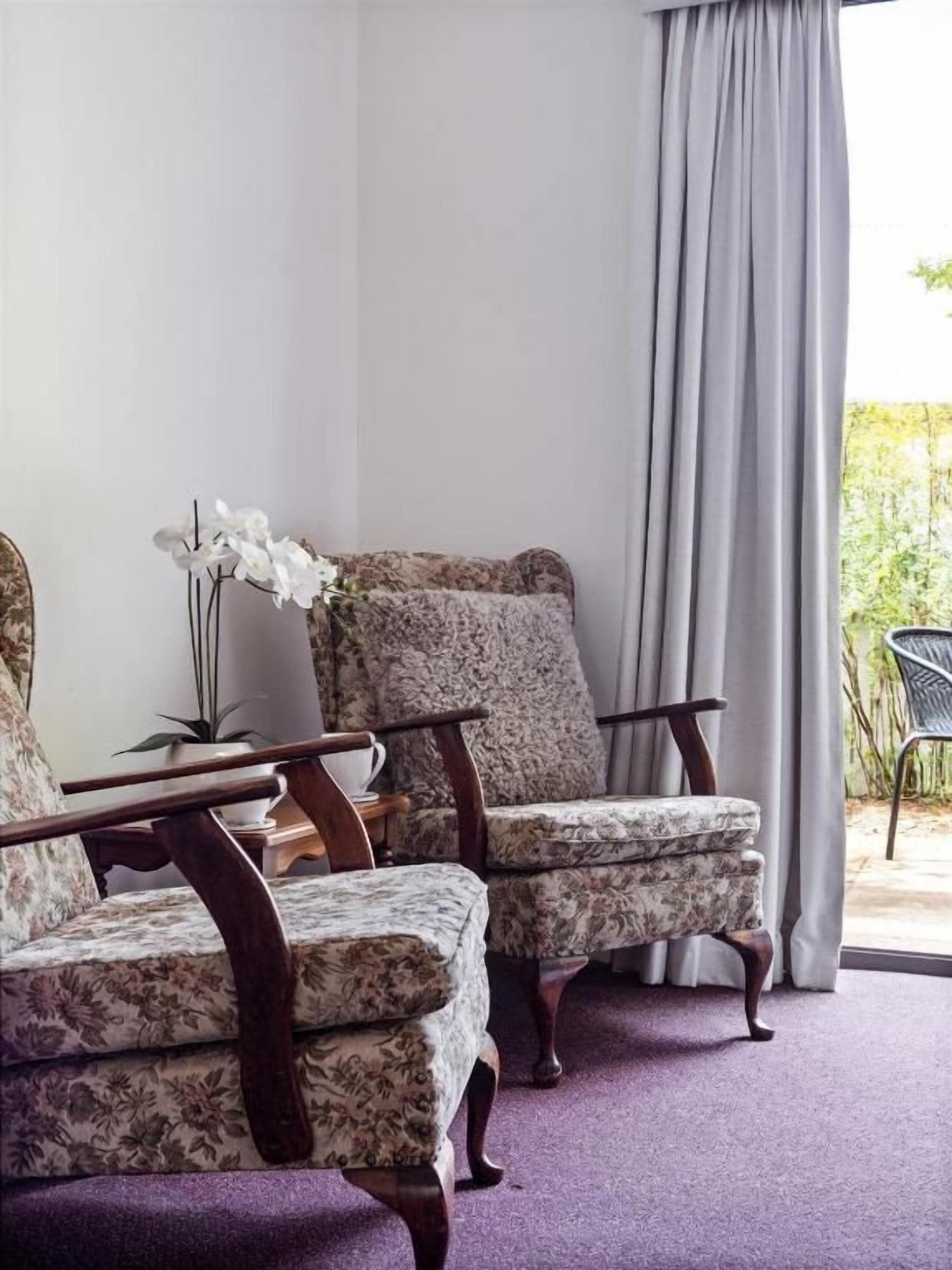 Une pièce comprenant deux fauteuils rembourrés à motifs floraux, une table d’appoint en bois et une plante en pot.