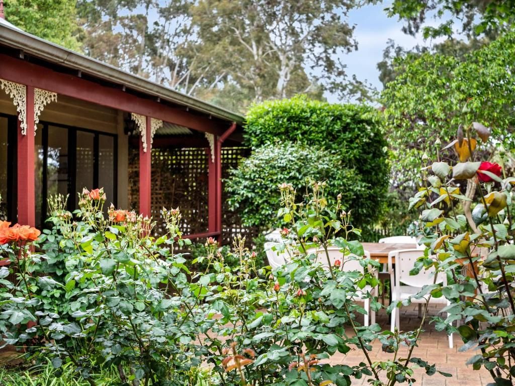 A garden with a red building, a white table, and a green hedge.