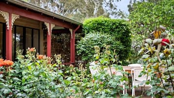 A garden with a red building, a white table, and a green hedge.