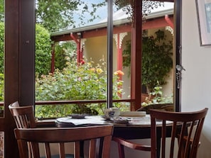 Un comedor con una mesa dispuesta para dos, una ventana con vistas a un jardín y una estructura de celosía roja.