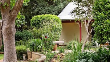 A garden with a variety of plants, a bench, and a building with a tiled roof.