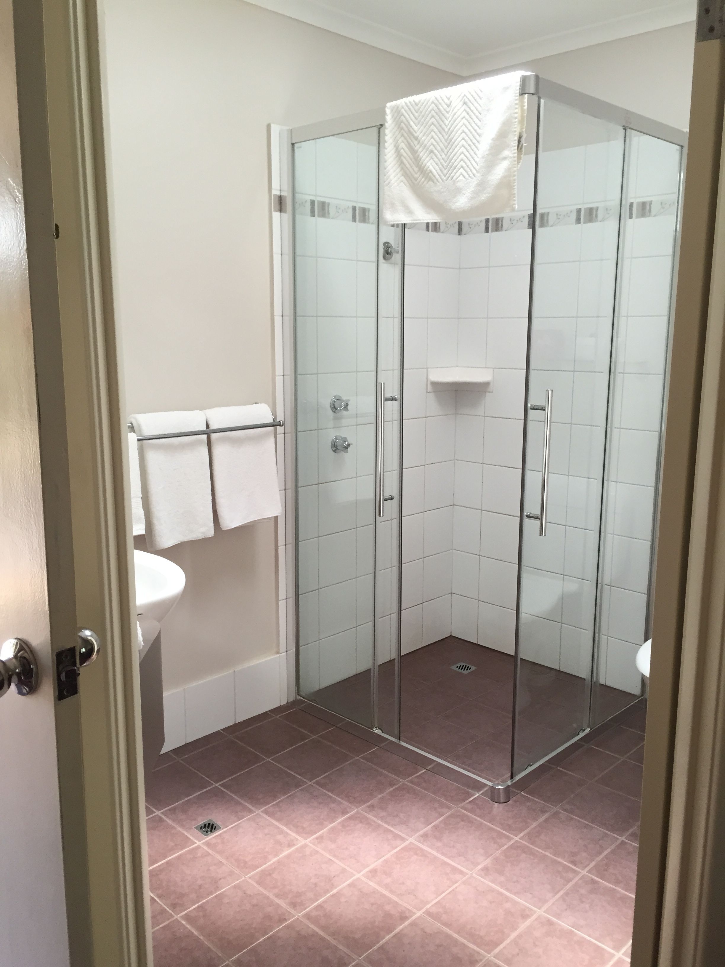 A glass-enclosed shower with a white towel hanging on a rack, a white sink, and a tiled floor.