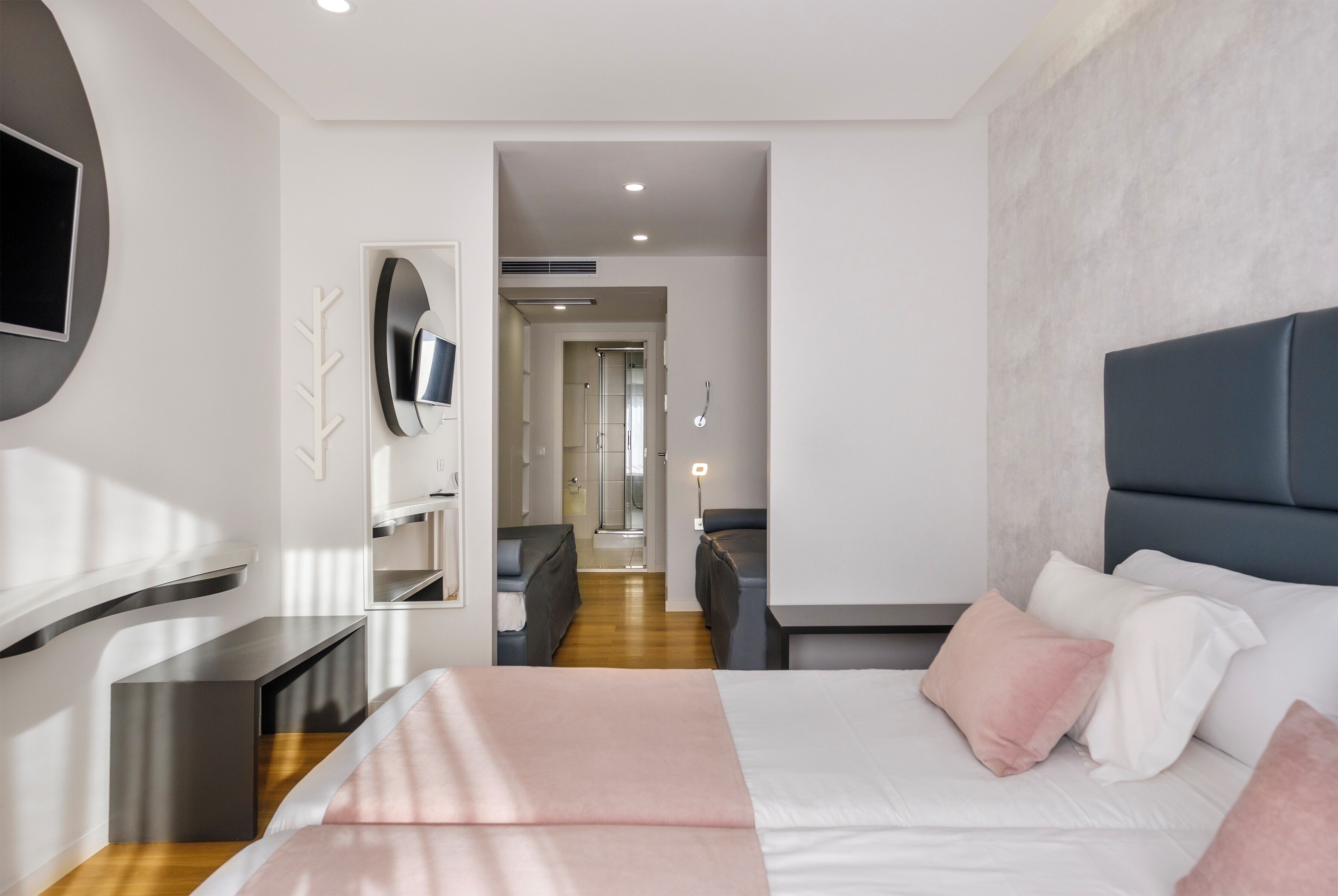 A modern hotel room with a bed, a TV, a desk, and a bathroom visible through an open door.
