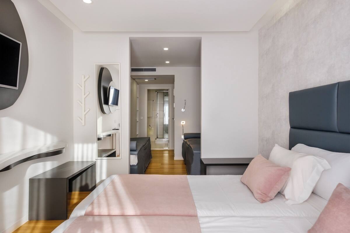 A modern hotel room with a large bed, a TV mounted on the wall, and a seating area with a sofa and chairs.