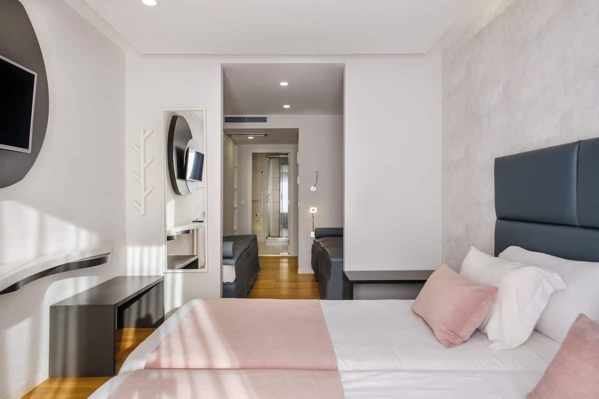 Ein modernes Hotelzimmer mit Bett, Fernseher, Schreibtisch und einem durchgehenden Türrahmen sichtbarem Badezimmer.