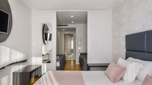 Une chambre d’hôtel moderne dotée d’un grand lit, d’un téléviseur fixé au mur et d’un coin salon avec un canapé et des fauteuils.