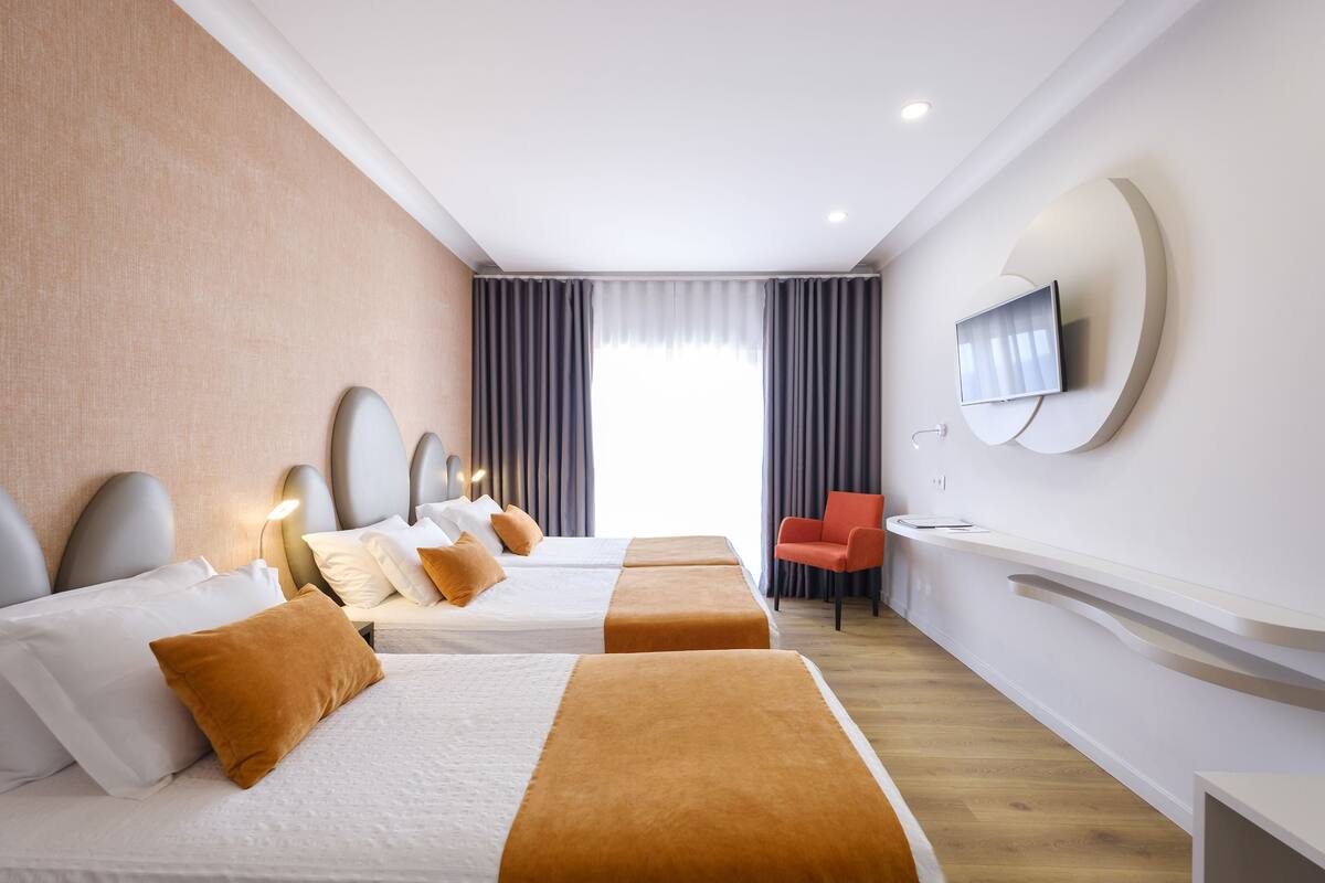 A hotel room with two beds, a TV mounted on the wall, a desk, and a chair.