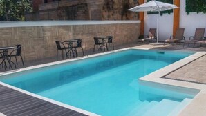 Une piscine rectangulaire avec une terrasse en bois et des chaises noires.